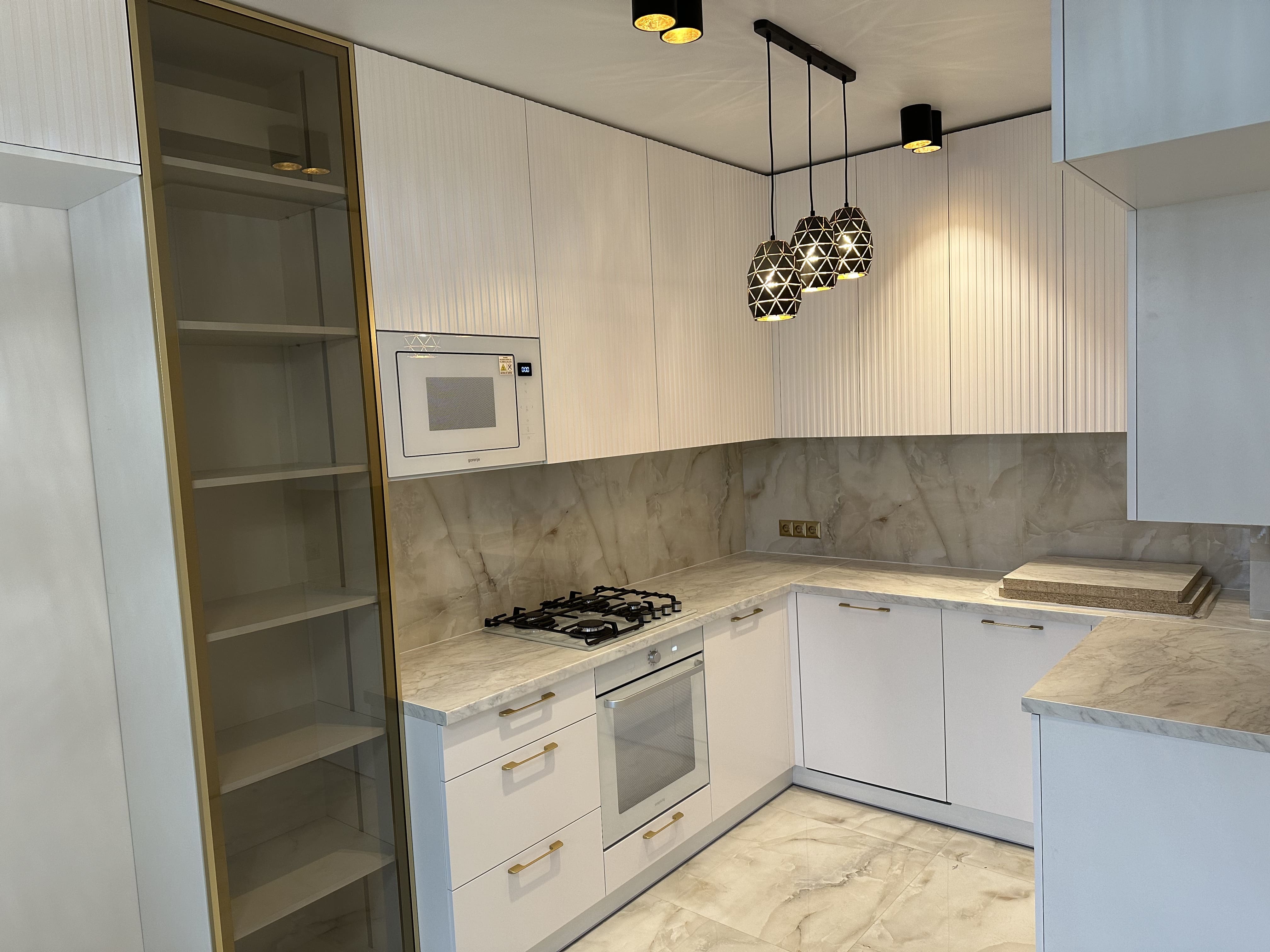 Біла стильна кухня з високою з золотою вітриною та золотими ручками